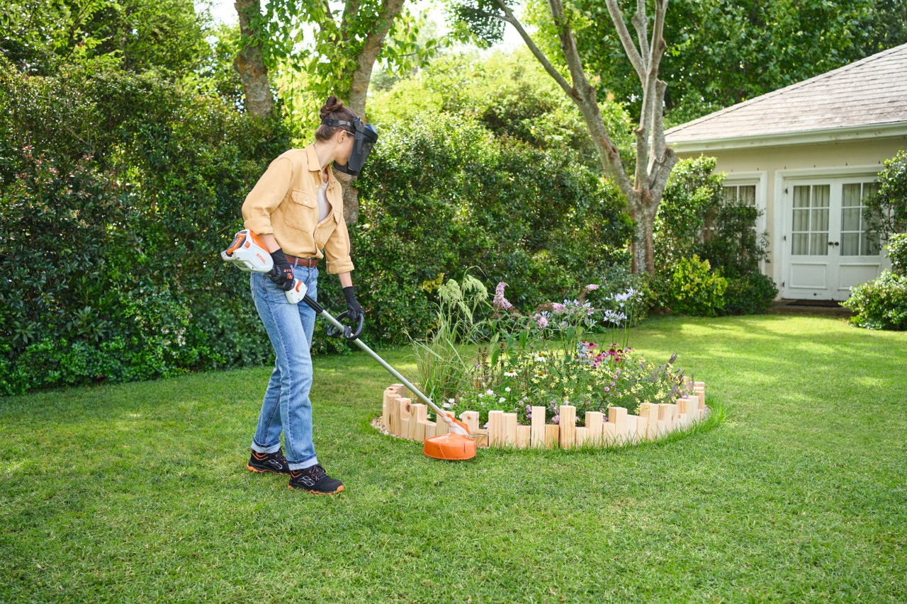 A woman cuts the tall grass around a bed border with the STIHL FSA 60 R brush cutter.